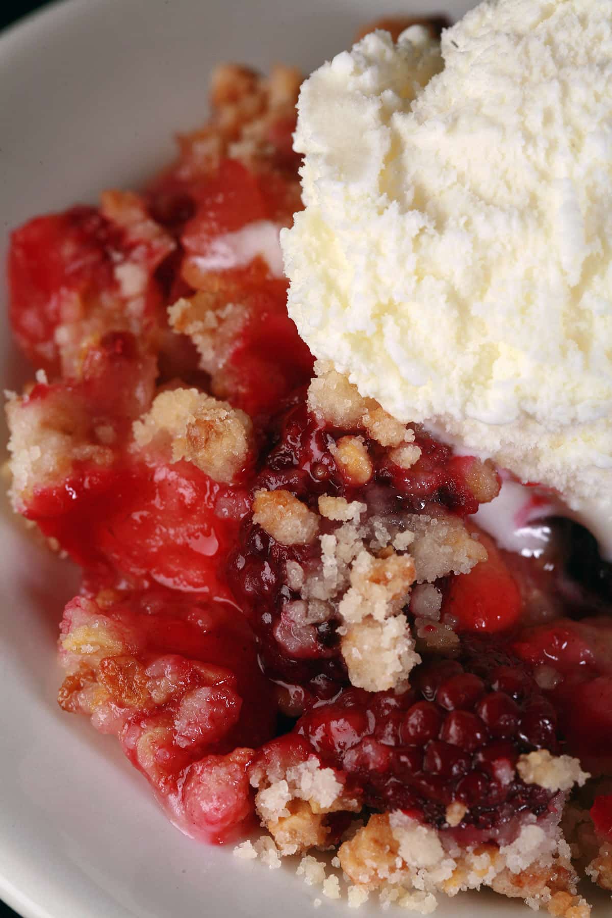 A serving of apple blackberry crumble topped with vanilla ice cream.