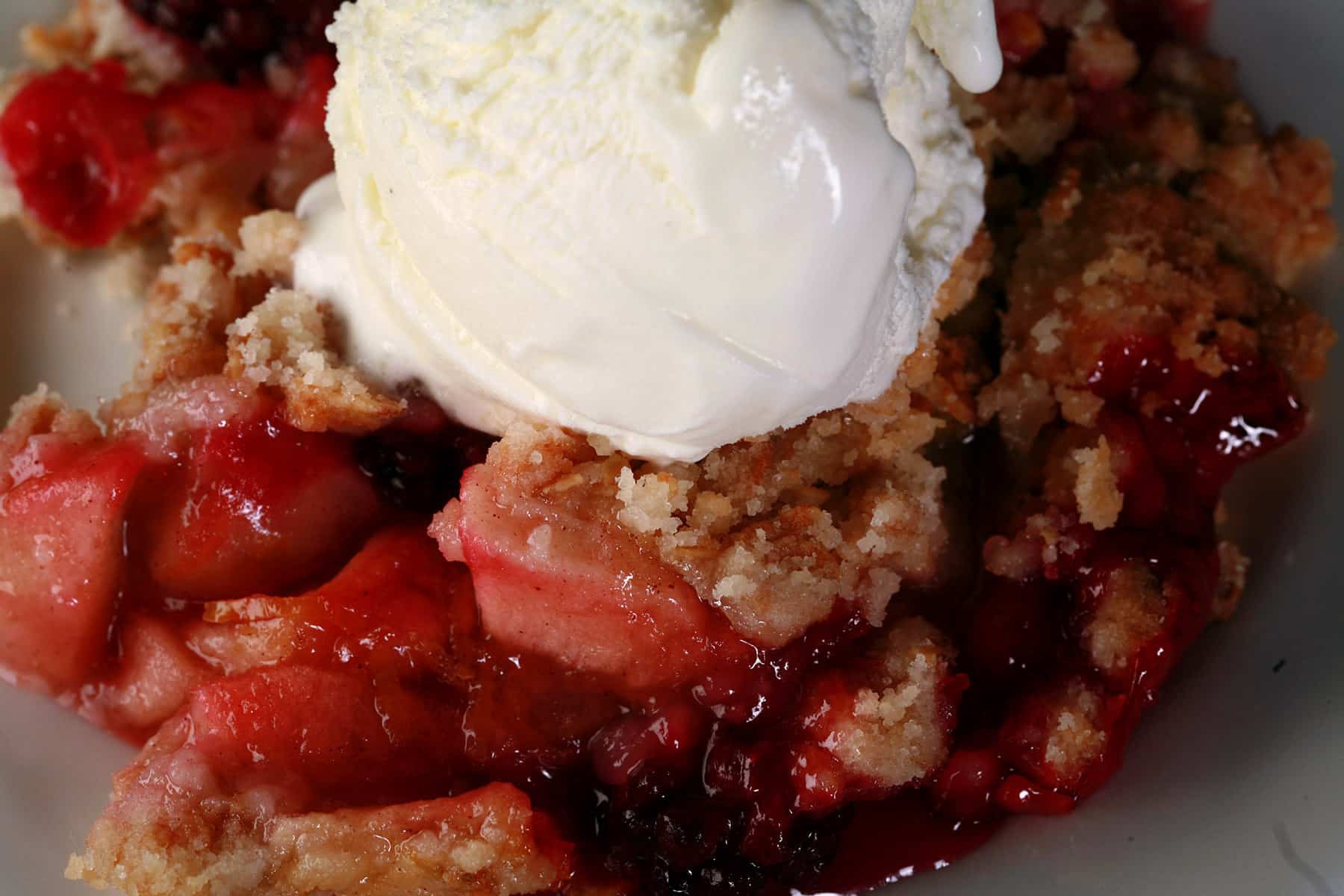 A serving of apple blackberry crumble topped with vanilla ice cream.