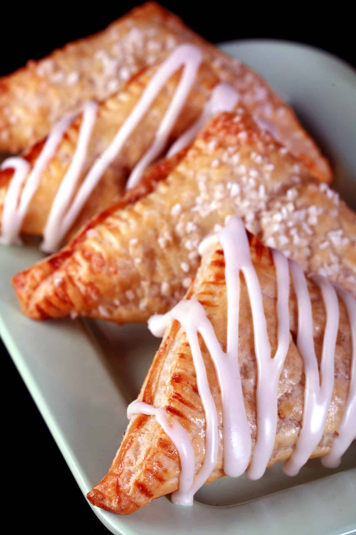 A plate of homemade apple turnovers, some with a drizzled glaze, the rest wth a chunky sugar crust.
