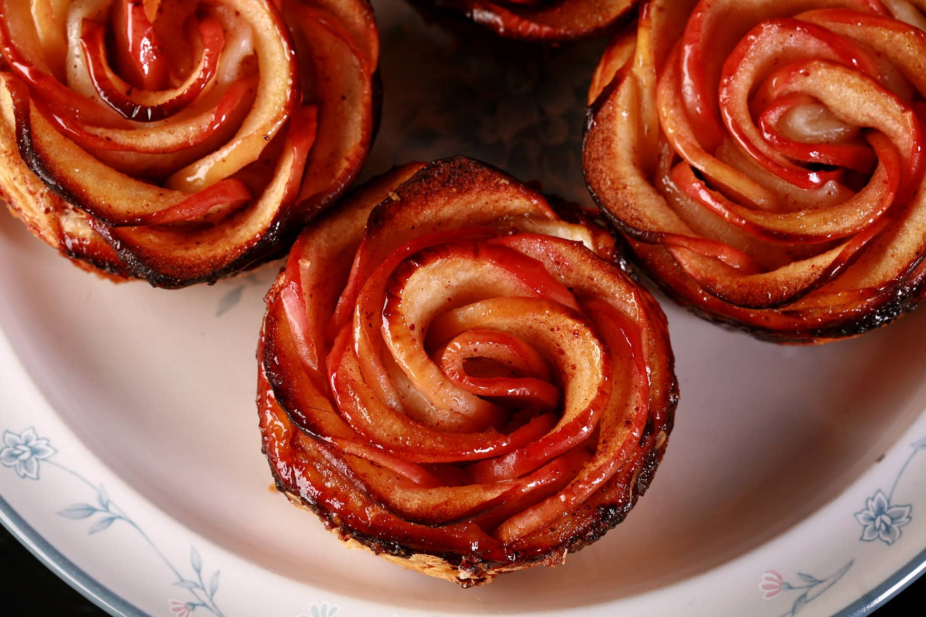 Maple syrup glazed apple roses with puff pastry, on a plate.