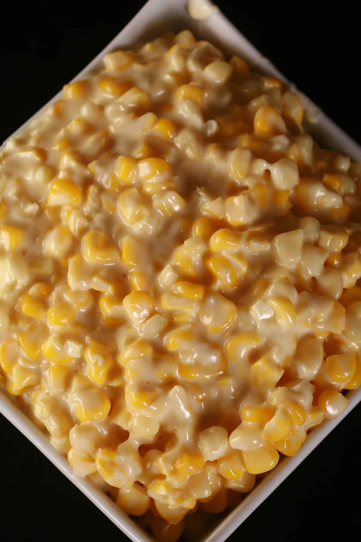 A white square bowl of homemade creamed corn.