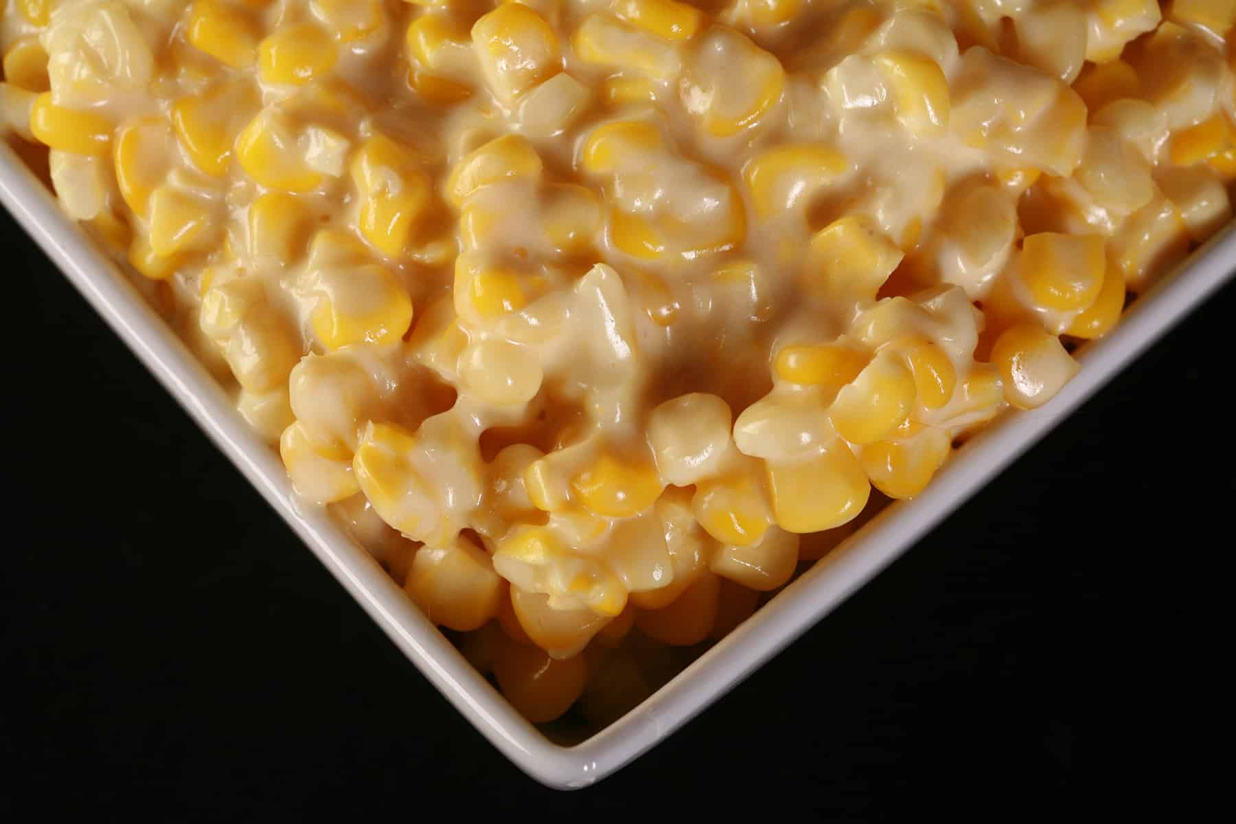A white square bowl of homemade creamed corn.