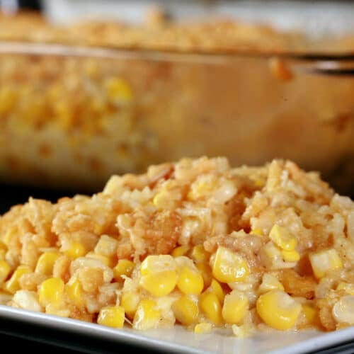 A plate of homemade scalloped corn in front of a glass bakinng dish with the rest of the casserole in it.