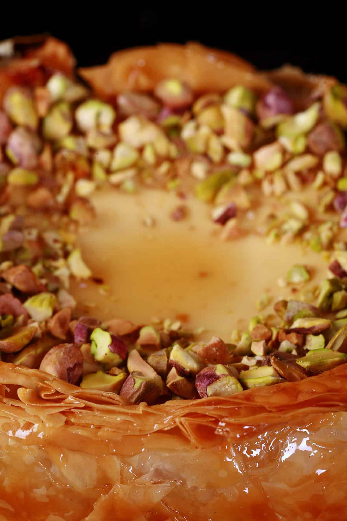A close upview of the top of a mini cheesecake, covered in chopped pistachios.