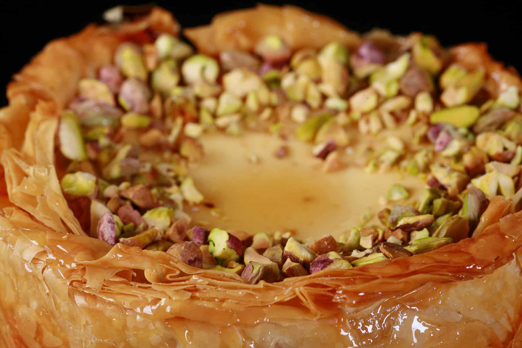 A close upview of the top of a mini baklava cheesecake, covered in chopped pistachios.