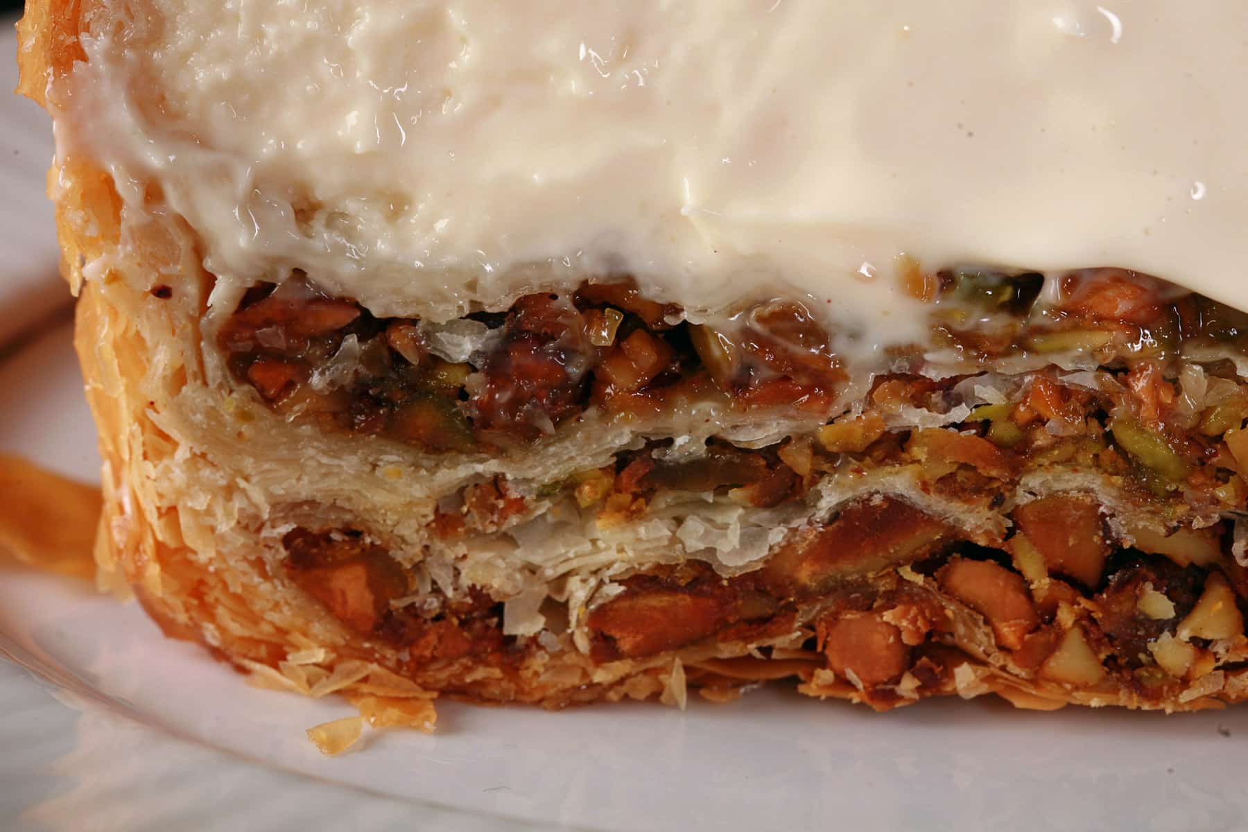 A close up view of the bottom of a slice of baklawa cheesecake, showing layers of pistachio baklava.