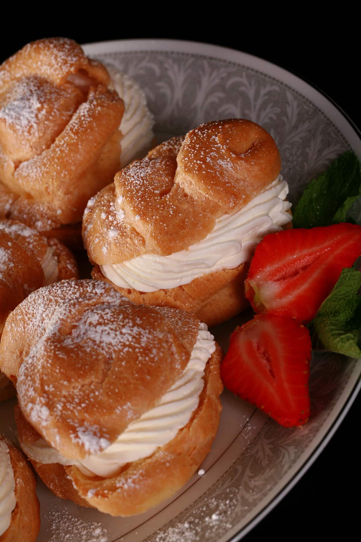A large plate of cream puffs, dusted with powdered sugar and garnished with strawberries..