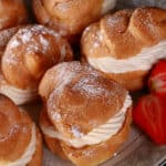 A large plate of cream puffs, dusted with powdered sugar and garnished with strawberries..