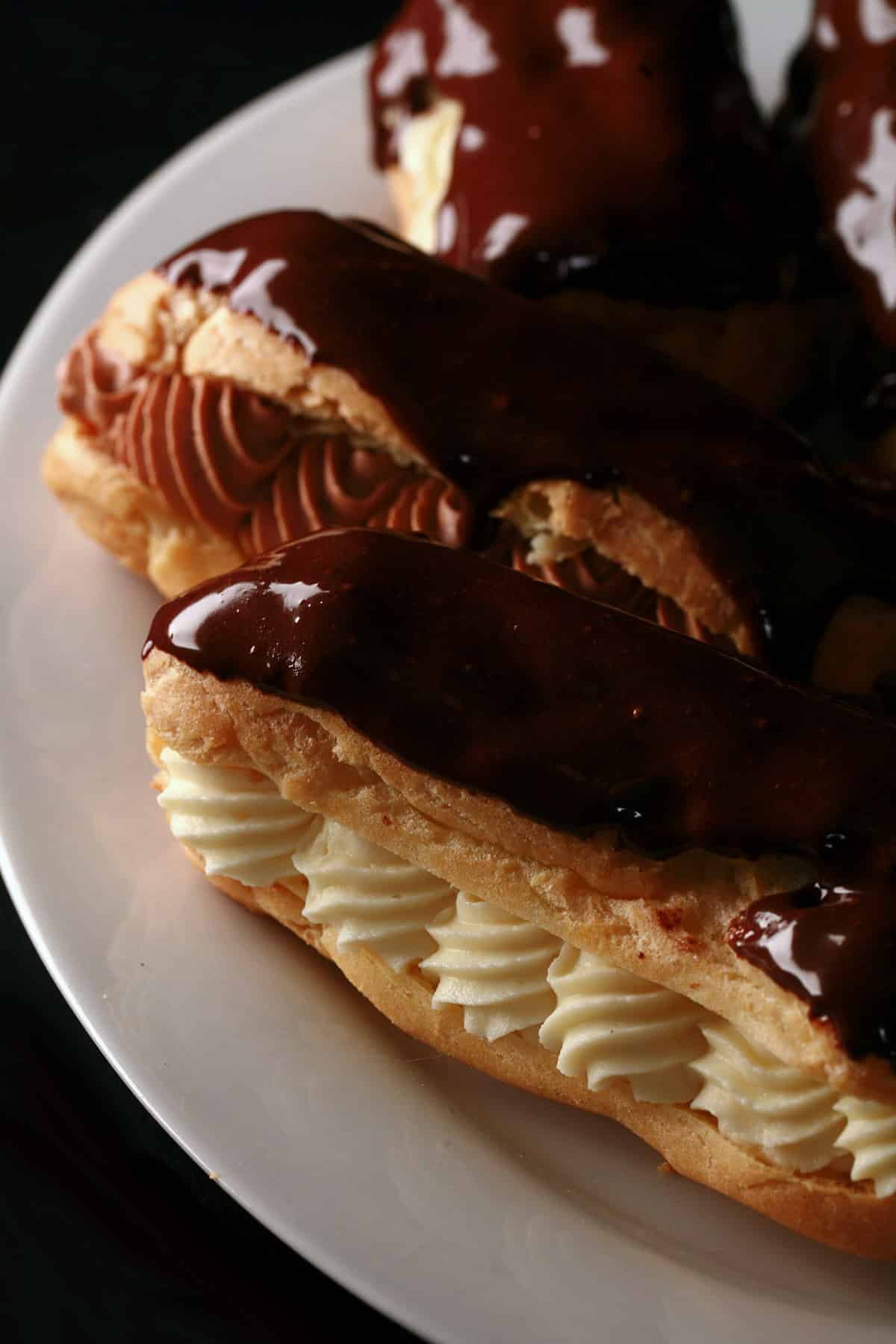 Several chocolate eclairs on a plate, with chocolate and vanilla cream fillings.