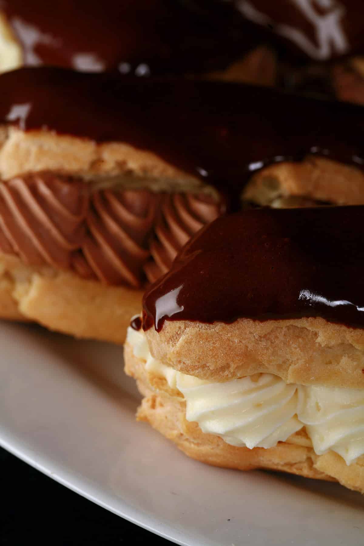 Several chocolate eclairs on a plate, with chocolate and vanilla cream fillings.