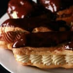 Several chocolate eclairs on a plate, with chocolate and vanilla cream fillngs.