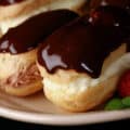 A plate of mini eclairs with chocolate and vanilla fillings and chocolate glaze.