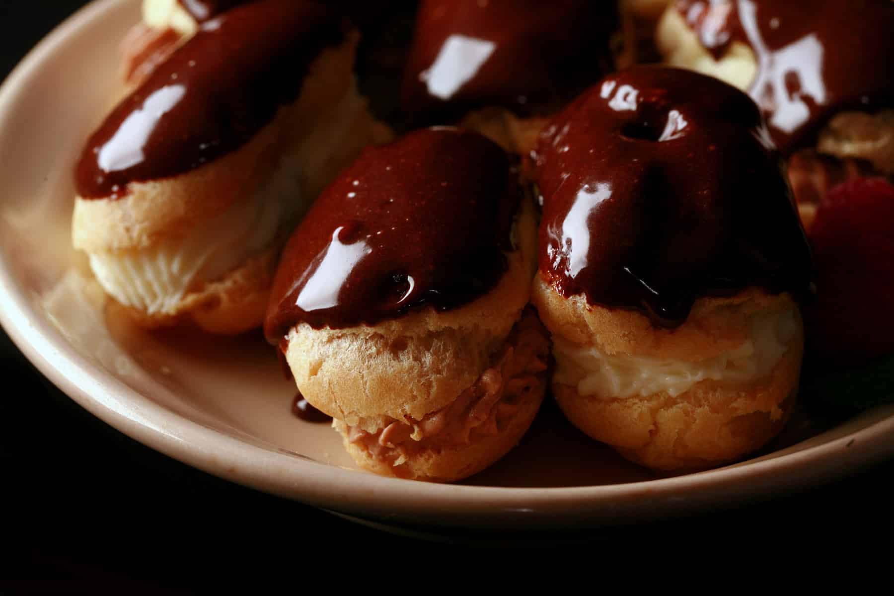 A plate of mini eclairs with chocolate and vanilla fillings and chocolate glaze.