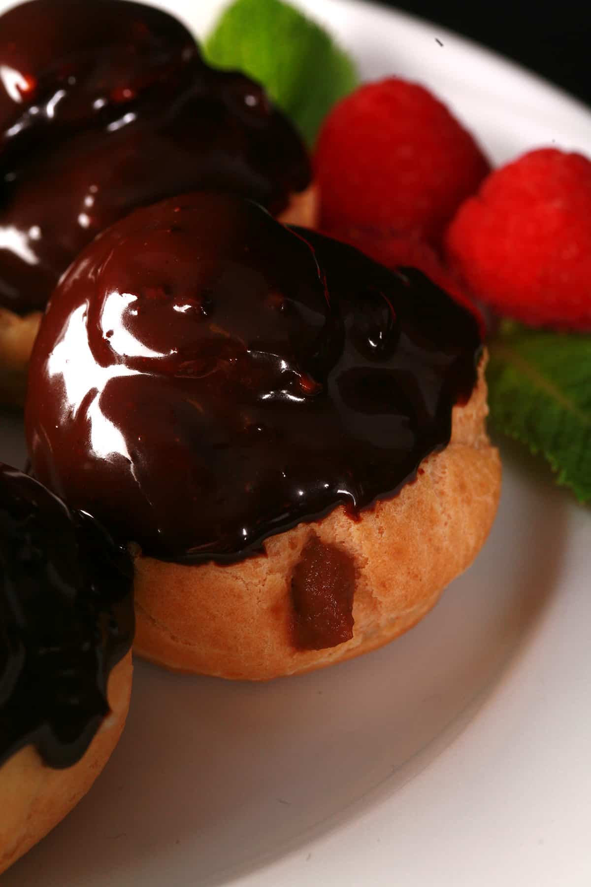 Several chocolate dipped profiteroles on a plate.
