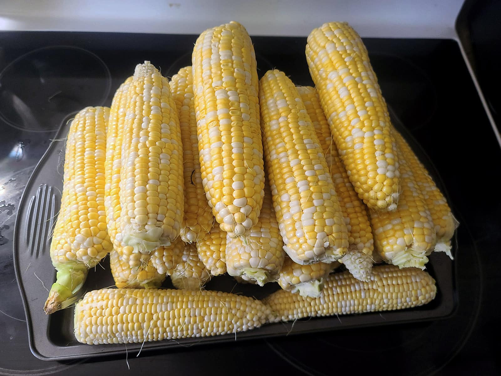 A pile of corn cobs on a white cuttiing board.