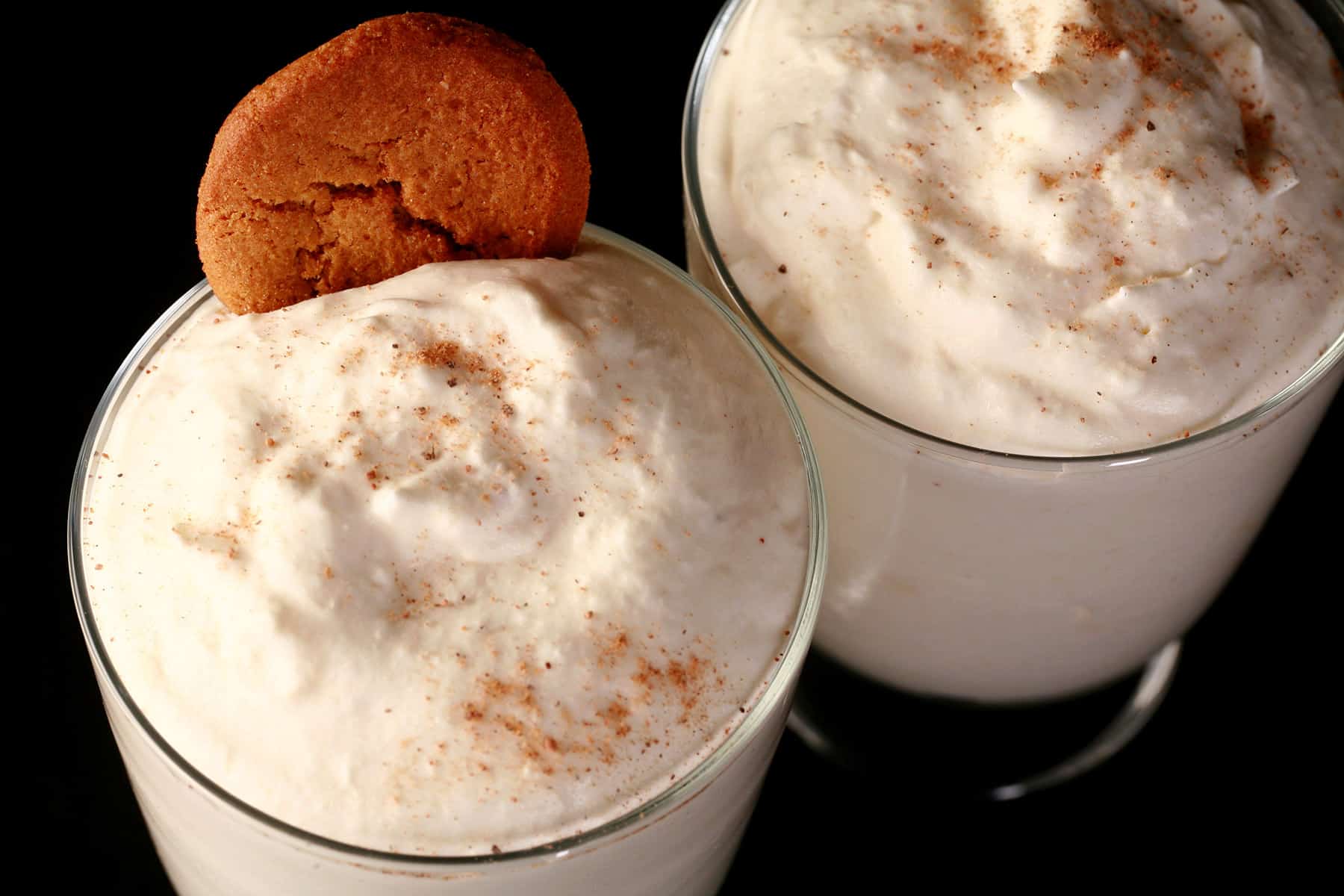2 glasses of traditional style eggnog mousse, with nutmeg and gingersnap cookie garnish.
