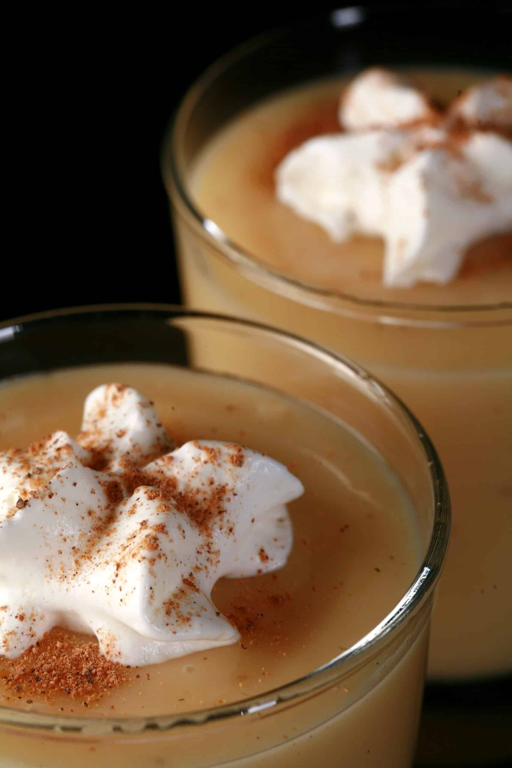 2 glasses of eggnog pudding, garnished with whipped cream and nutmeg.