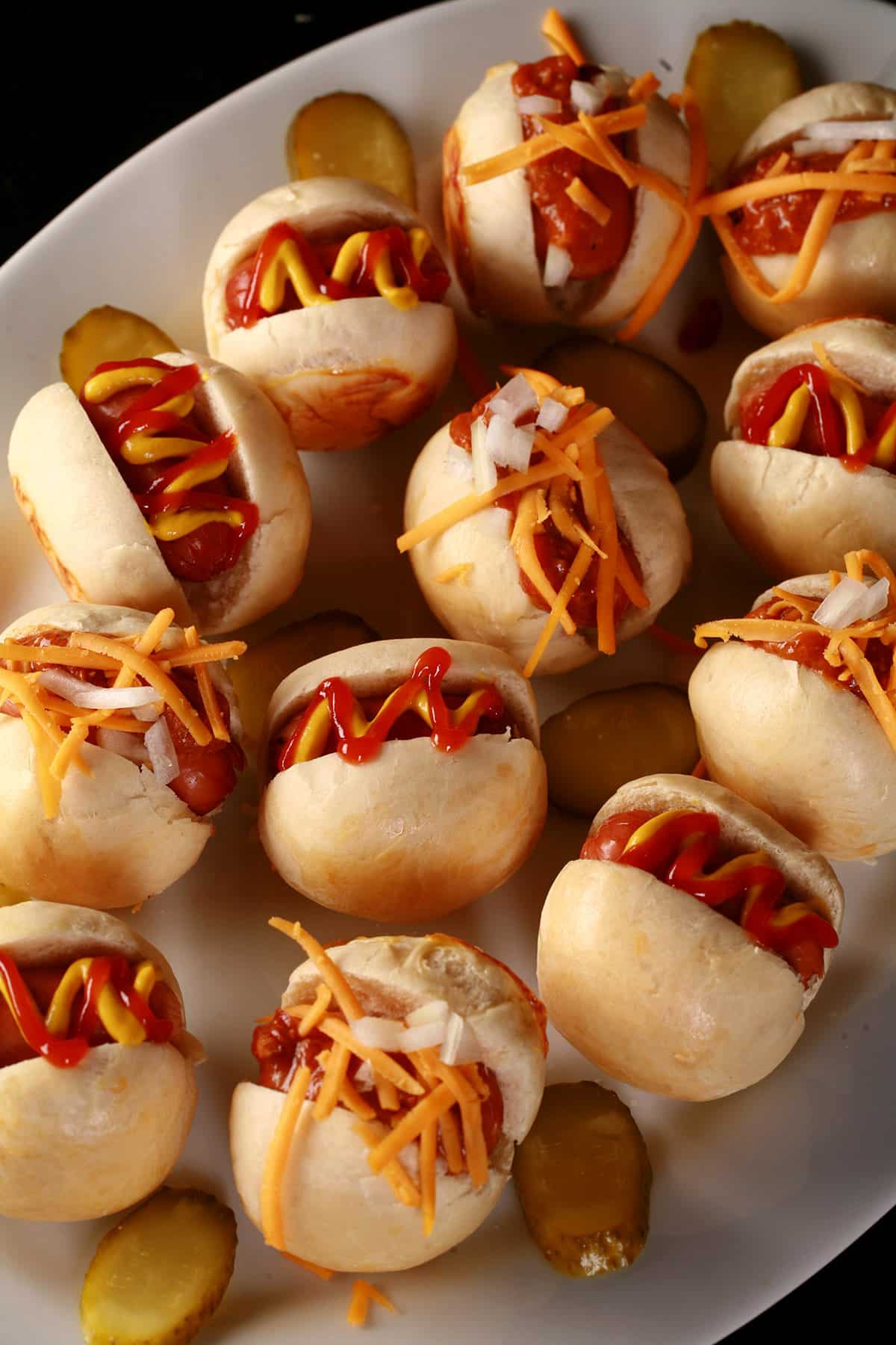 A plate of hot dog sliders, with cheese, hot dog, ketchup, and chili toppings.