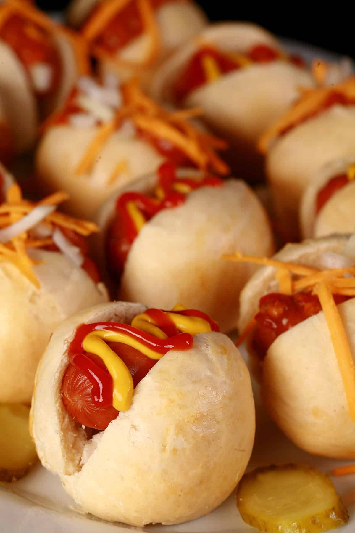 A plate of hot dog sliders, with cheese, hot dog, ketchup, and chili toppings.