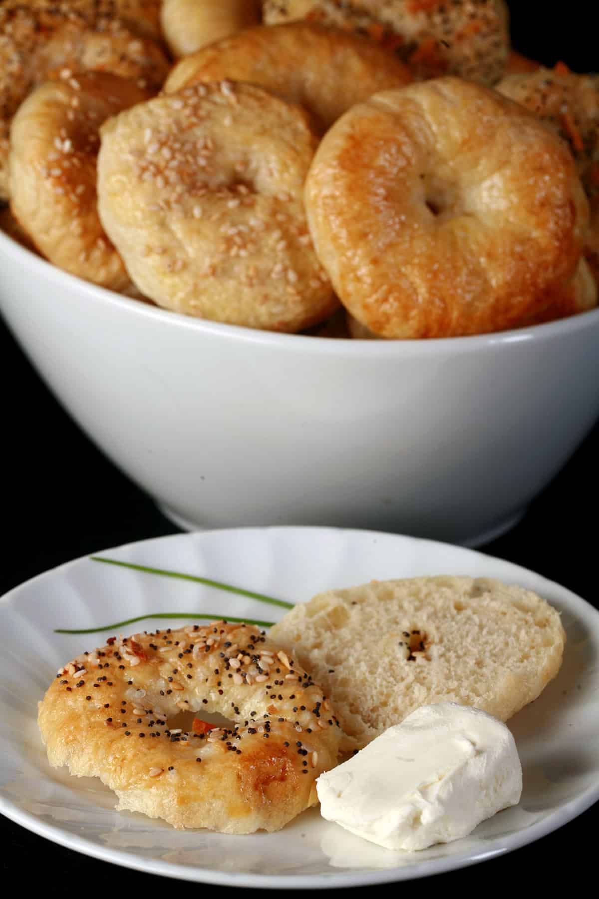 A sliced mini bagel on a plate, with a bowl of mini bagels behind it.