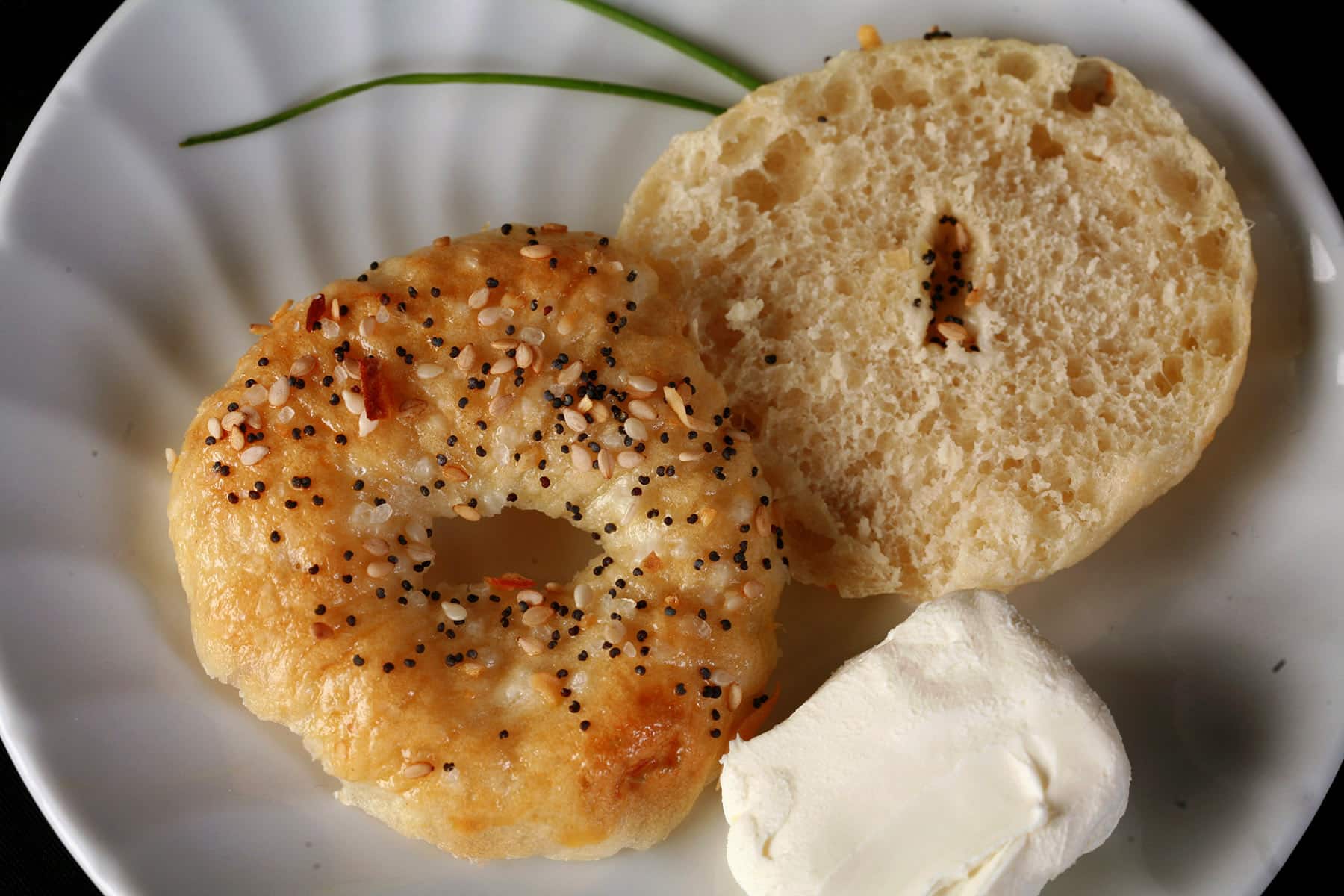 A sliced mini bagel on a plate, with some cream cheese next to it.