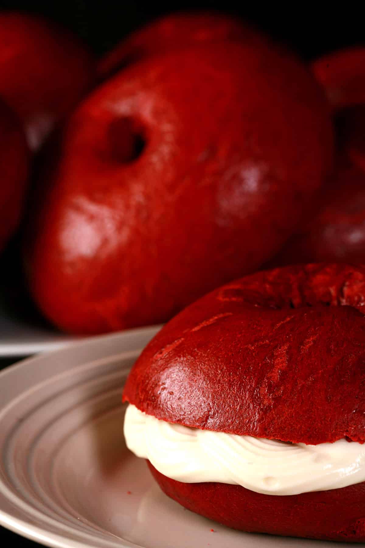 A plate of homemade red velvet bagels, with a sliced red velvet bagel with cream cheese filling in front.