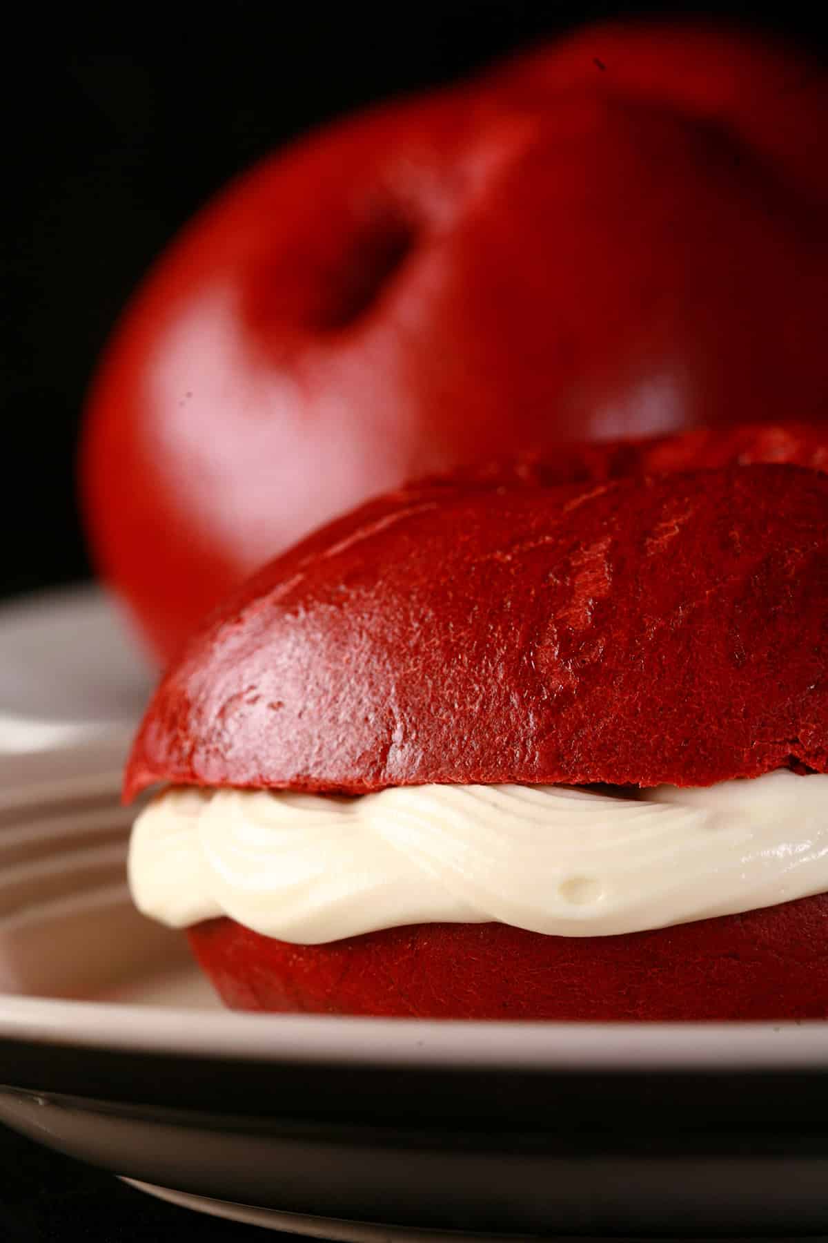 A plate of homemade red velvet bagels, with a sliced red velvet bagel with cream cheese filling in front.