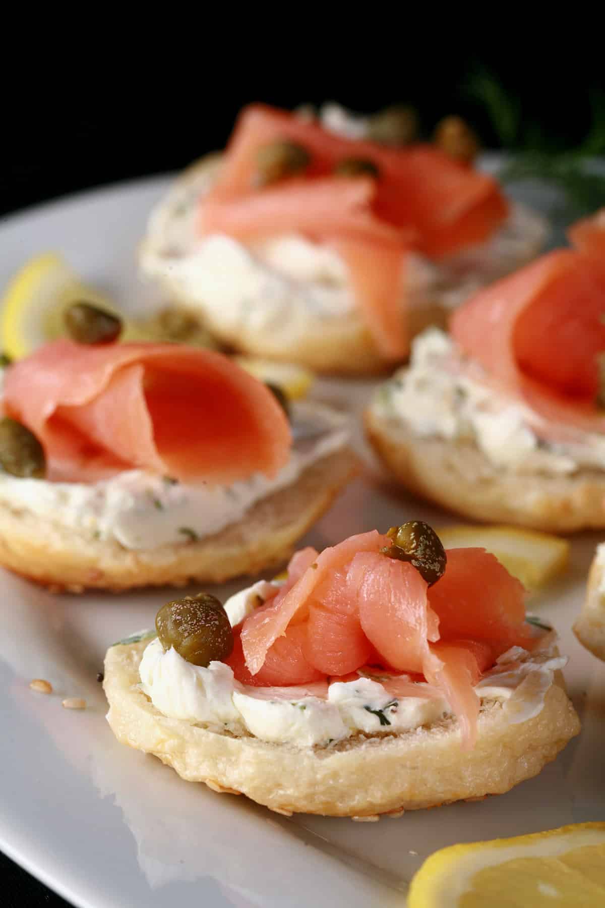 A platter of smoked salmon bagel bites garnished with capers and lemon slices.