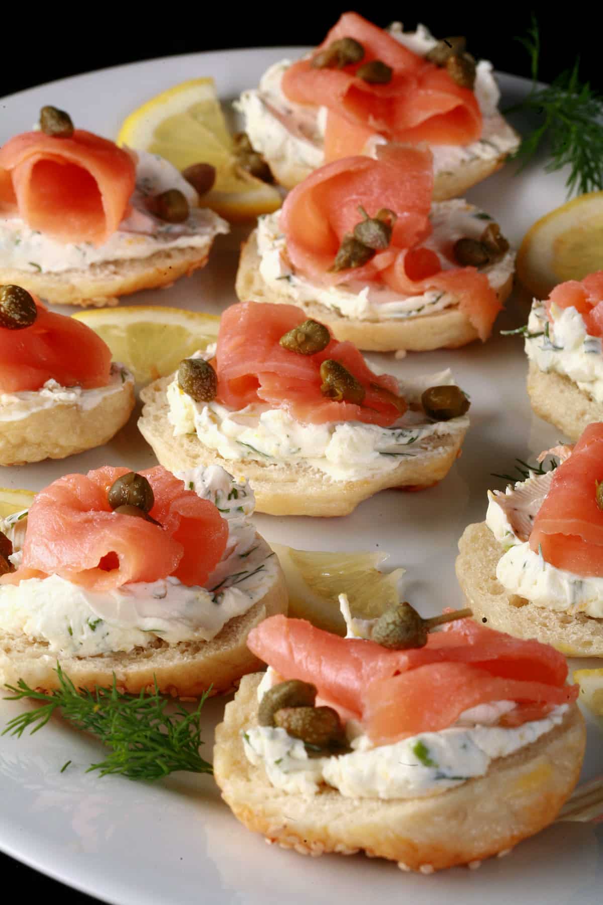 A platter of smoked salmon bagel bites garnished with capers and lemon slices.