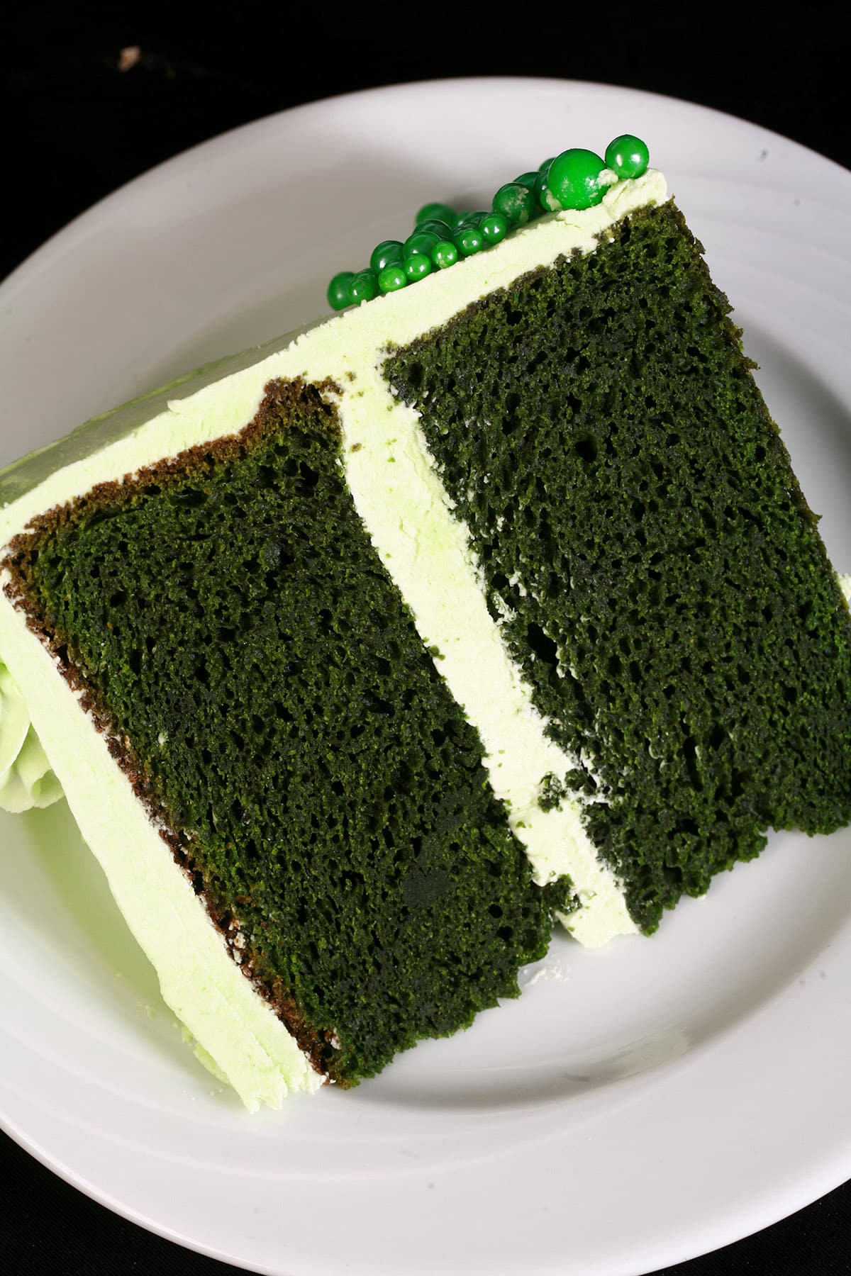 A slice of green velvet cake with light green frosting on a white plate.