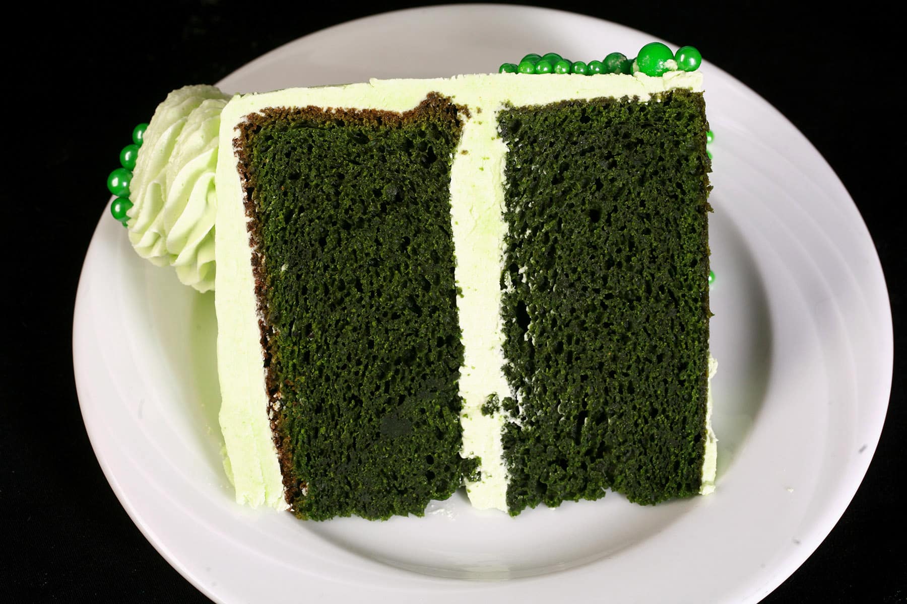 A slice of green velvet cake with light green frosting on a white plate.