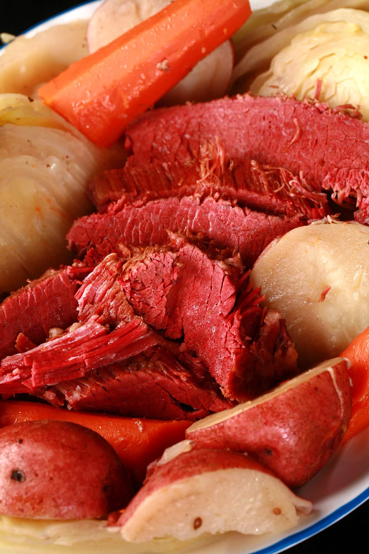 A close up view of some homemade corned beef brisket, nestled among boiled cabbage, carrots, and potatoes.
