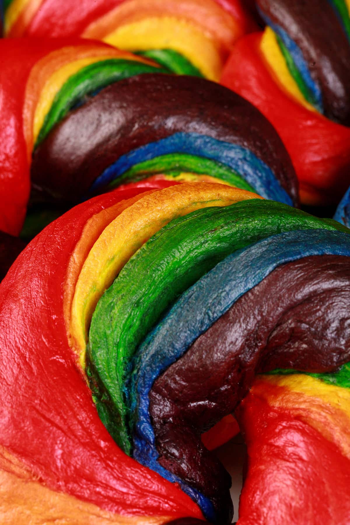 A close up photo of 2 brightly colored rainbow twist bagels.