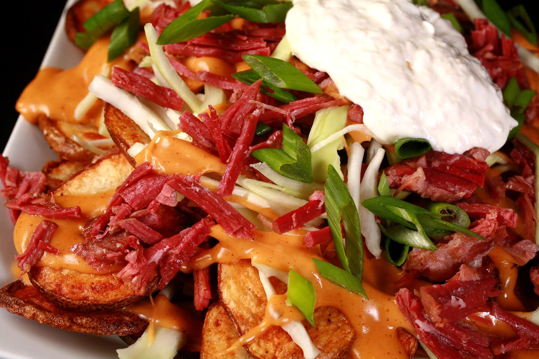 A close up photo of a plate of St Patrick’s Day nachos - baked potato slices, Guinness cheese sauce, cabbage, corned beef, green onions, and horseradish sour cream.