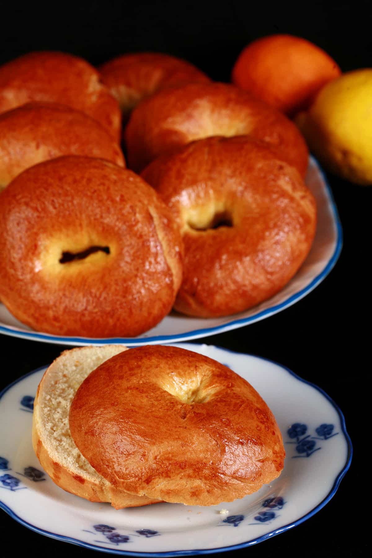 A plate of paska bagels with a sliced bagel, a lemon, and an orange beside it.