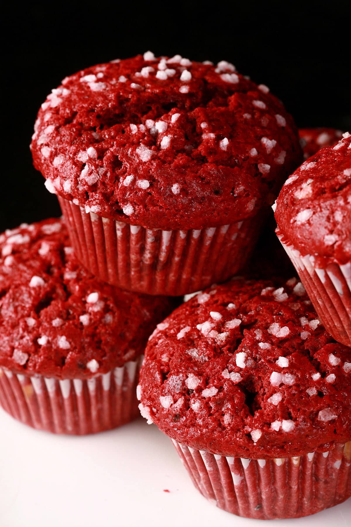 A pile of red velvet muffins on a plate, each topped with pearl sugar.