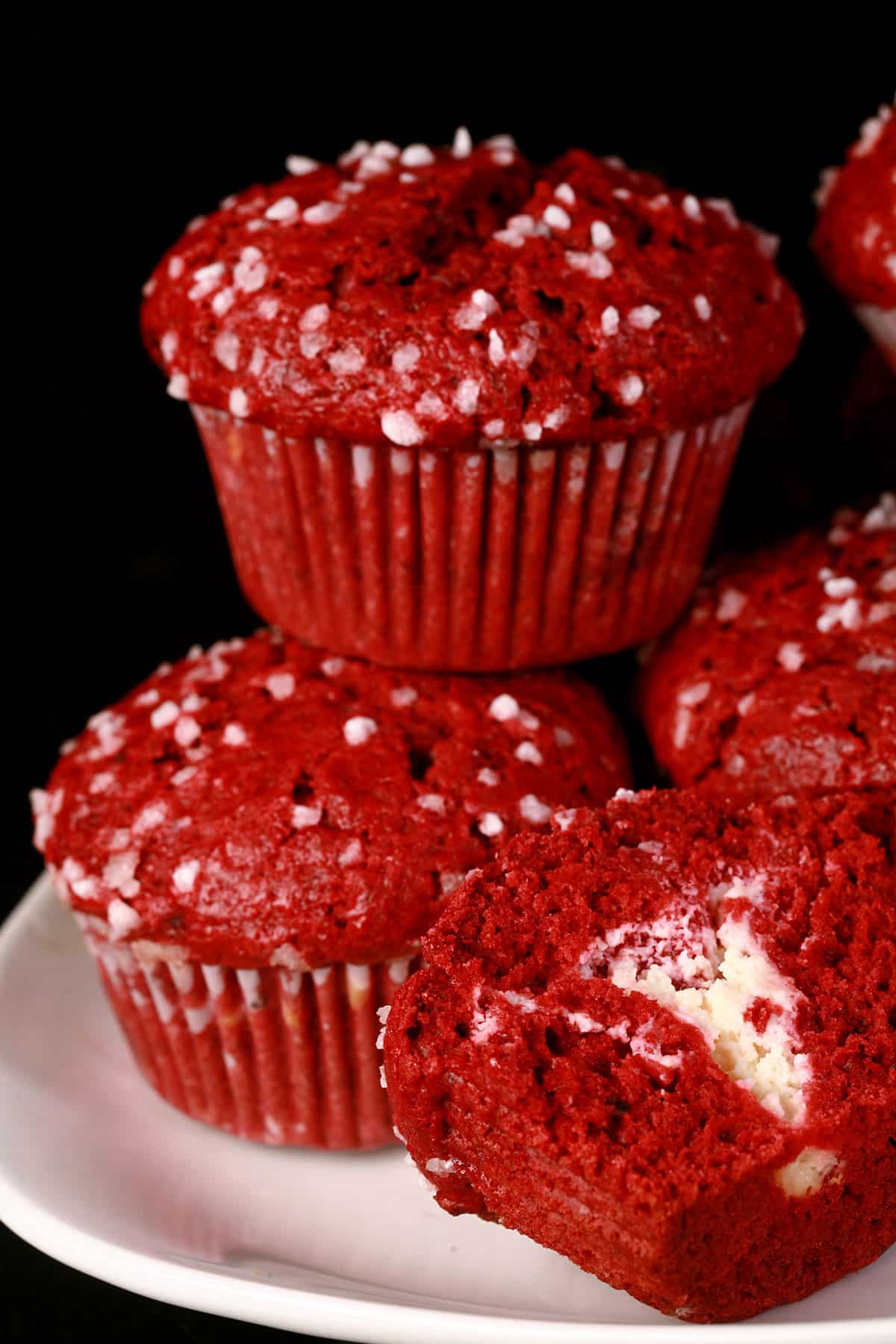 A cut open red velvet muffin with cream cheese filling, with more red velvet muffins behind it.