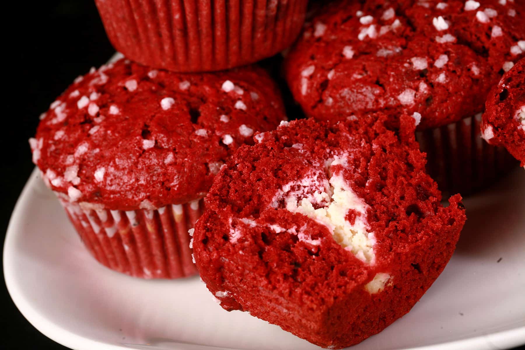 A cut open red velvet muffin with cream cheese filling, with more red velvet muffins behind it.