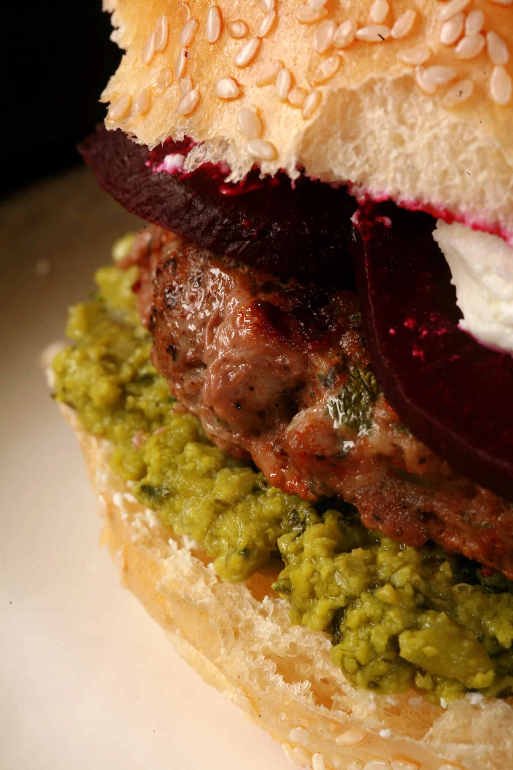 A close up photo of a moroccan spiced lamb burger with pea hummus, goat cheese, and roasted beets.