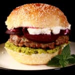 A close up photo of a moroccan lamb burger with pea hummus, goat cheese, and roasted beets.