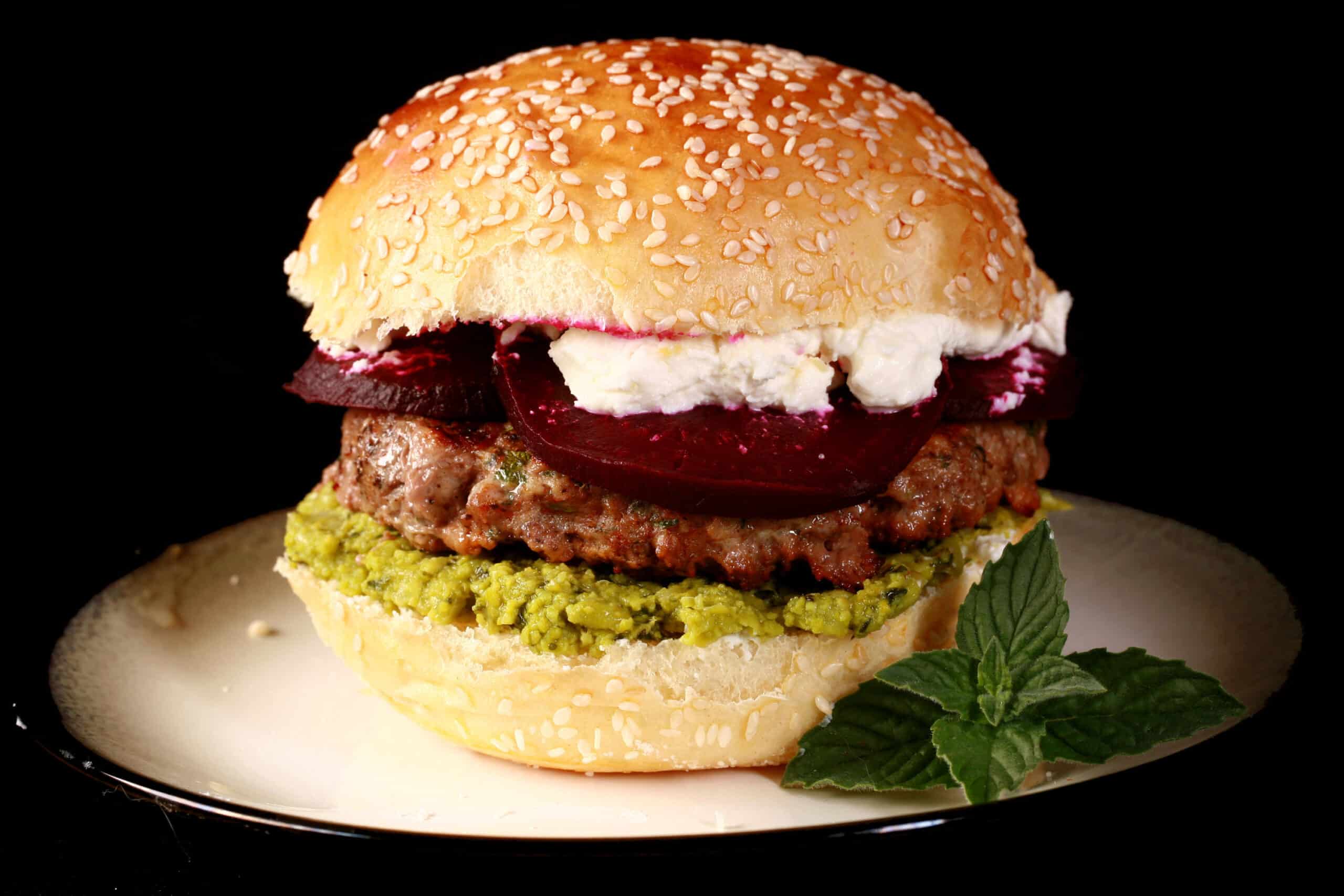 A close up photo of a moroccan lamb burger with pea hummus, goat cheese, and roasted beets.
