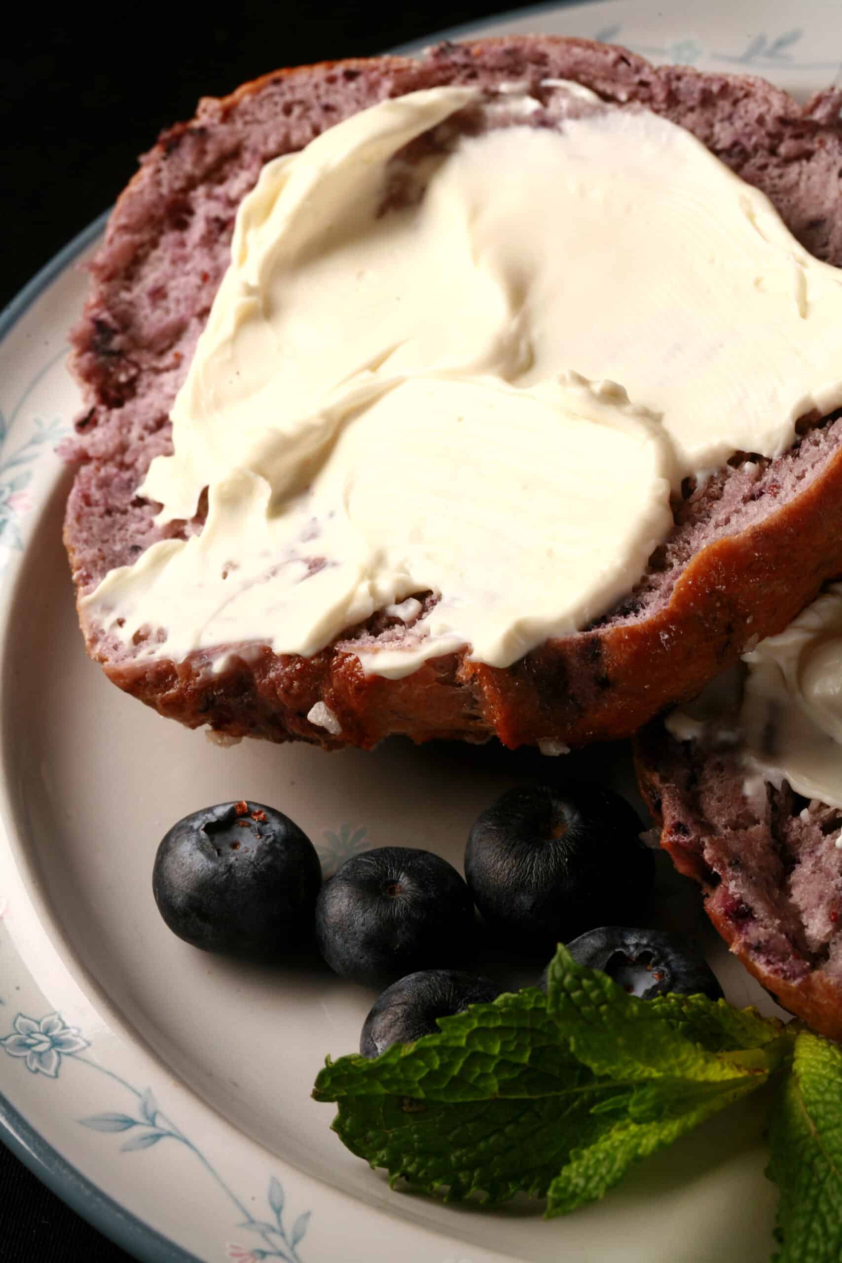 A split open blueberry bagel, spread with cream cheese.