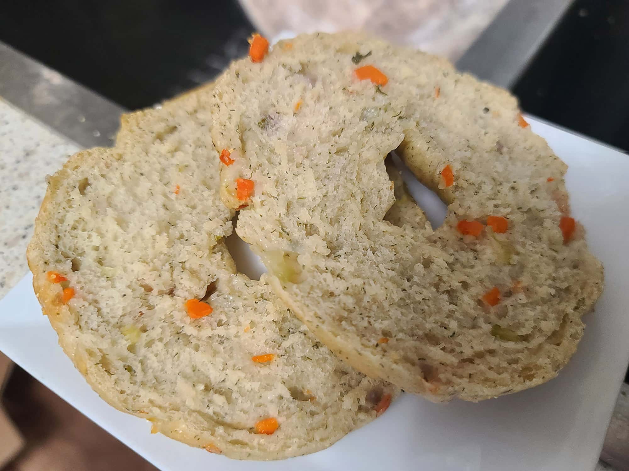 A close up few of a cut open vegetable bagel.  the herbs and pieces of vegetables can be clearly seen throughout.