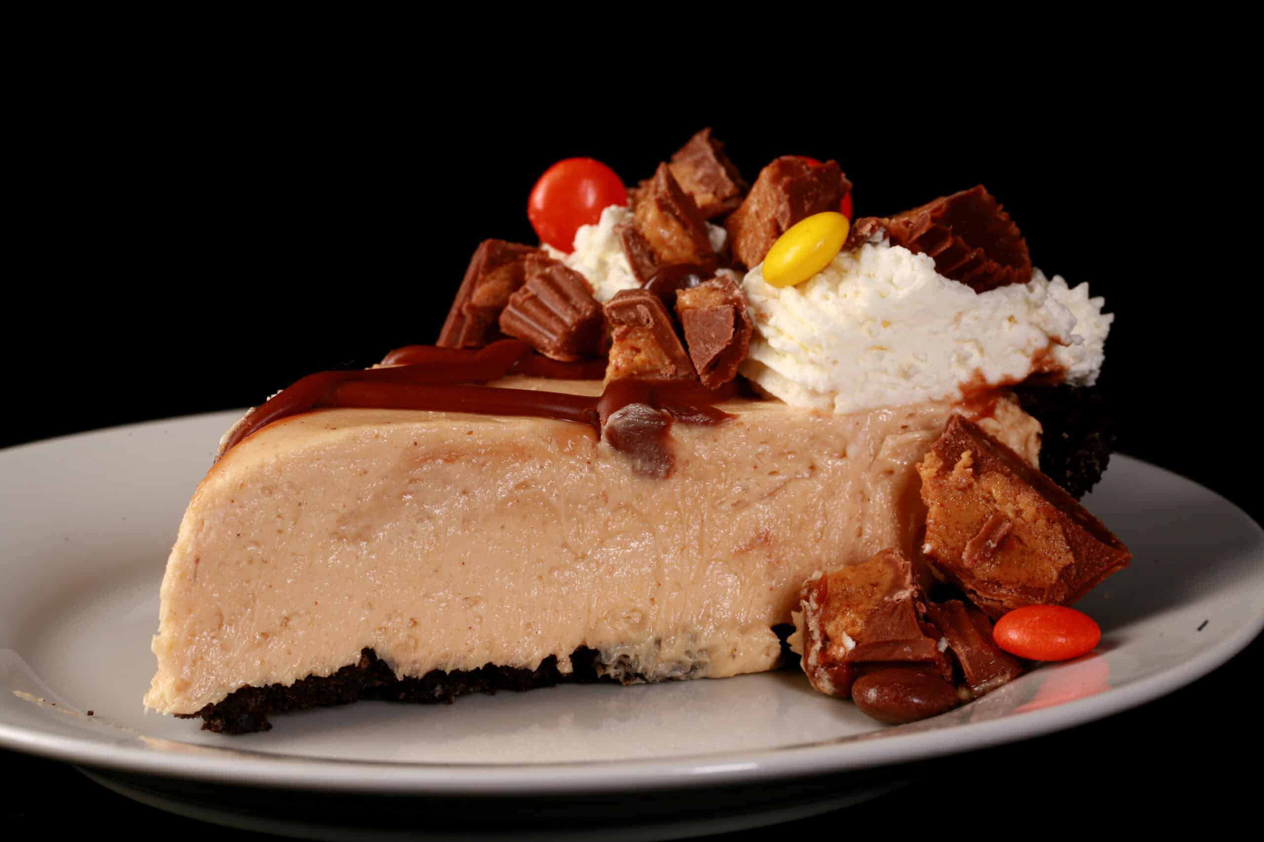 A slice of Reese’s Peanut Butter Pie, with chocolate lattice top,  whipped cream rosettes, chopped peanut butter cups, and Reese’s Pieces.