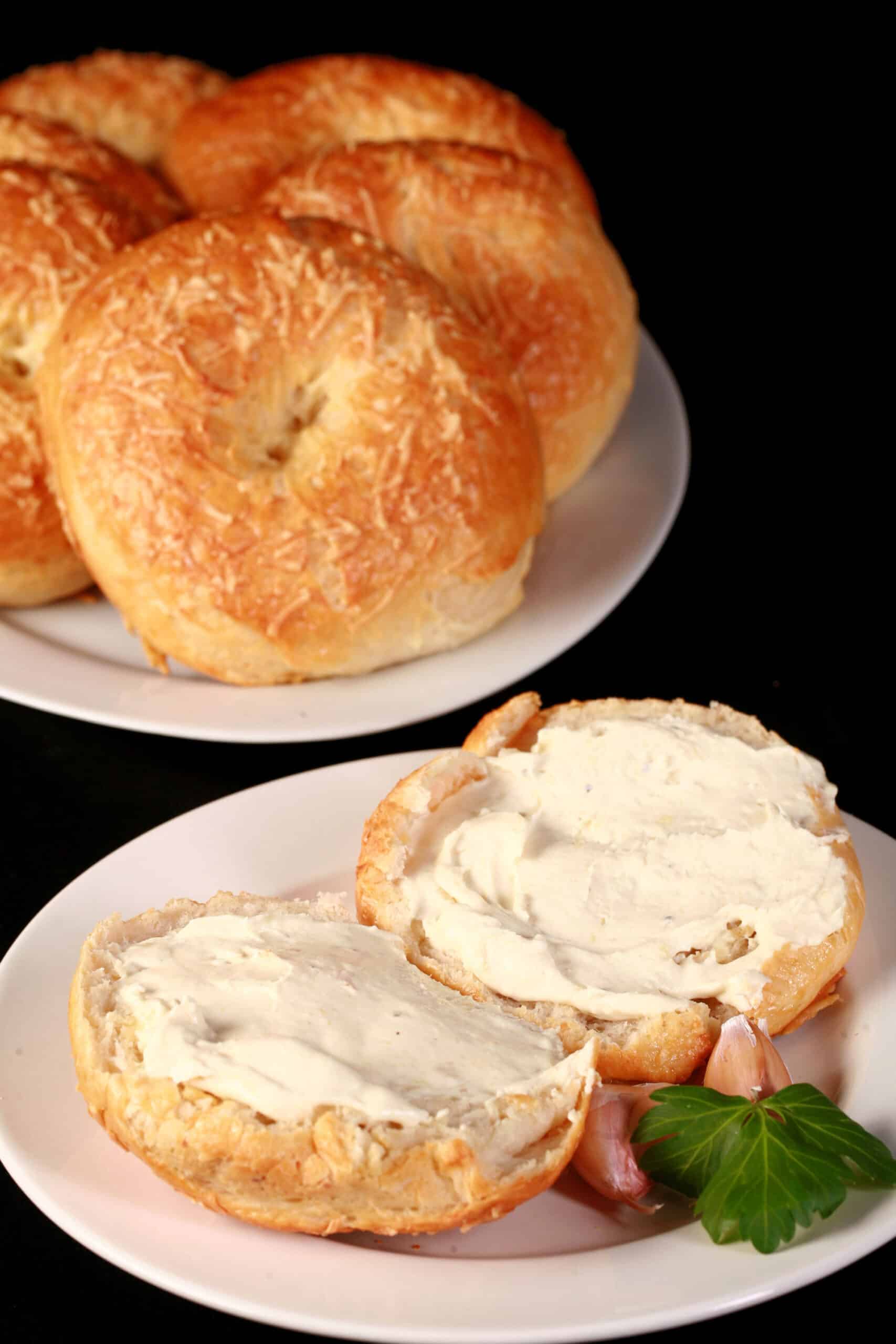 A split open roasted garlic asiago cheese bagel with cream cheese on it in front of a plate of asiago bagels.