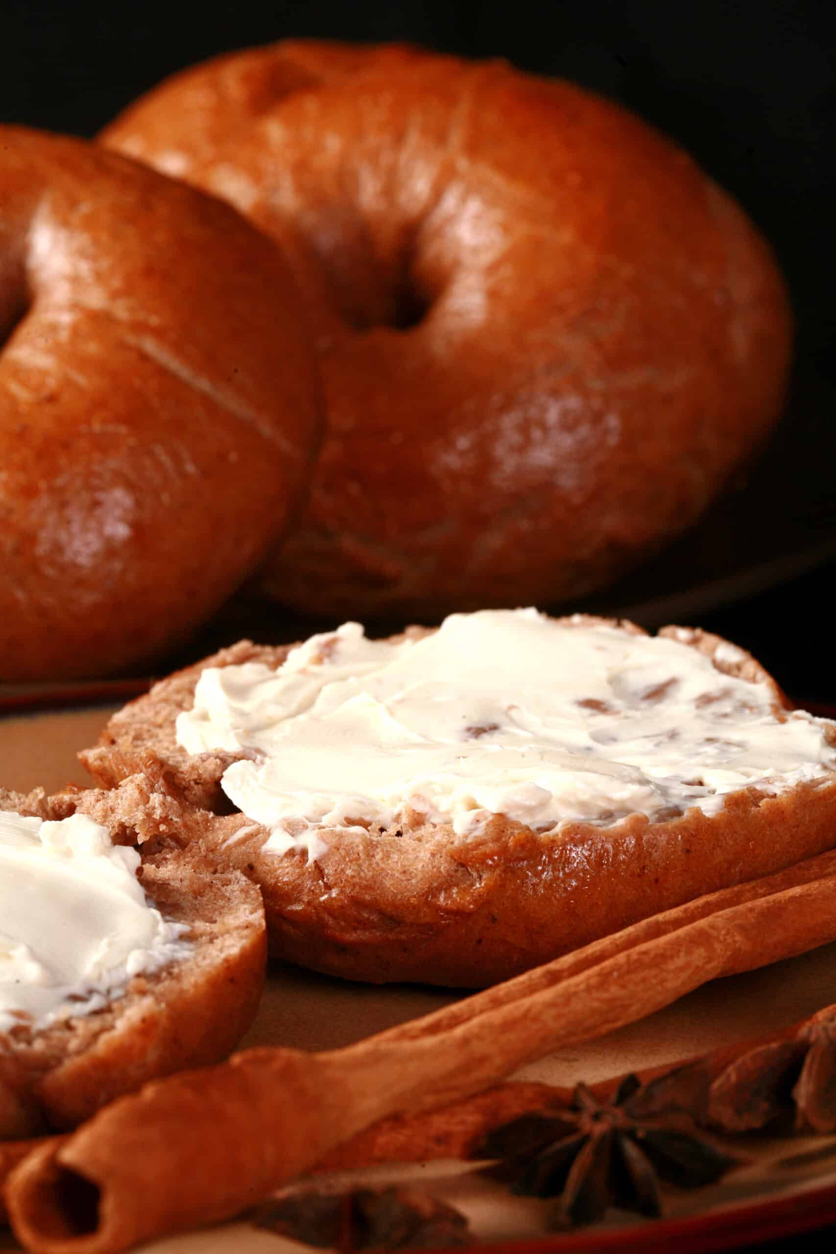 A split open chai bagel spread with cream cheese, in front of a plate of chai spiced bagels.