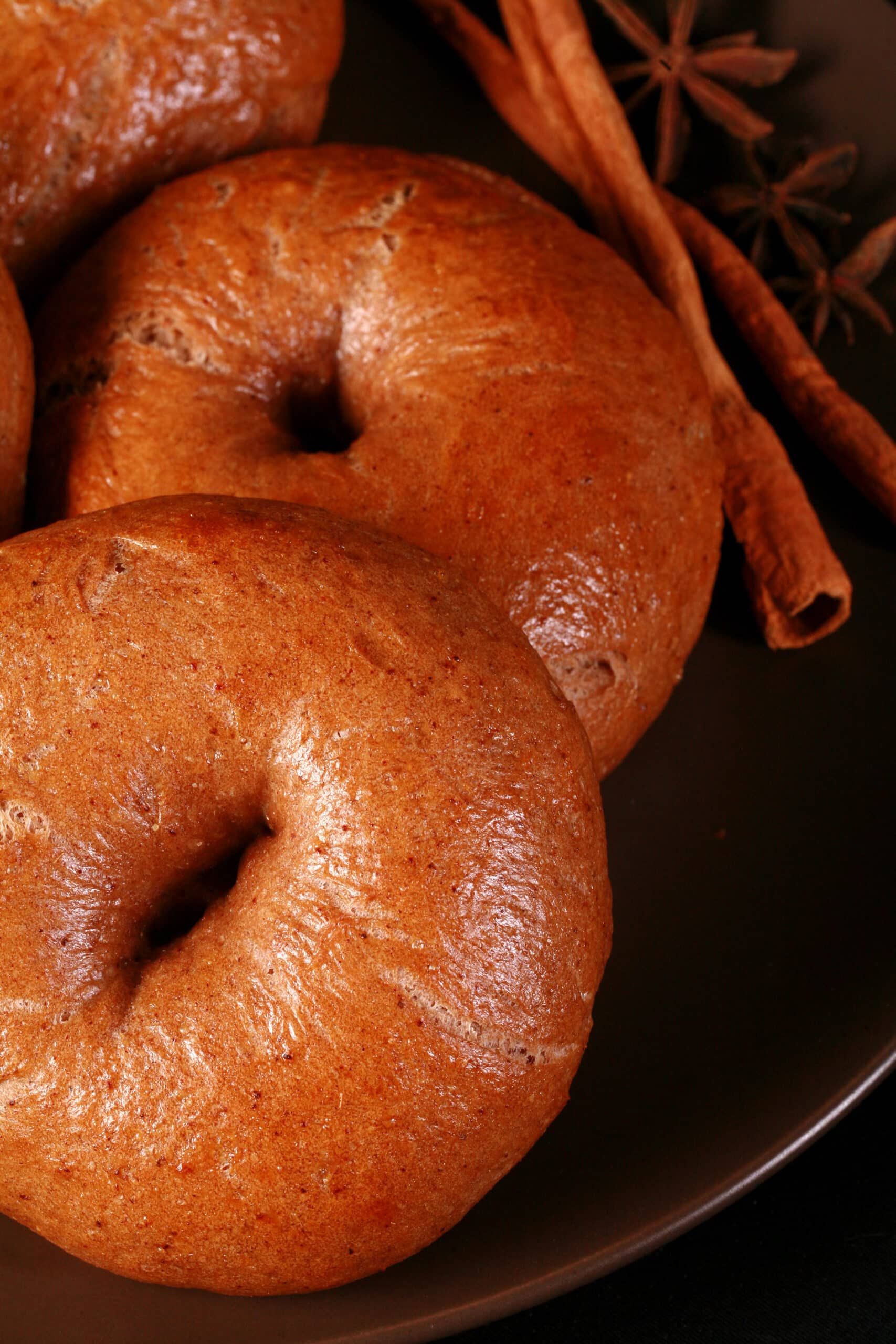 A plate of spiced chai bagels with cinnamon sticks and star anise on the side.