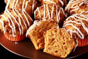 A plate of sweet potato muffins with pecan streusel topping and vanilla glaze drizzled on top.