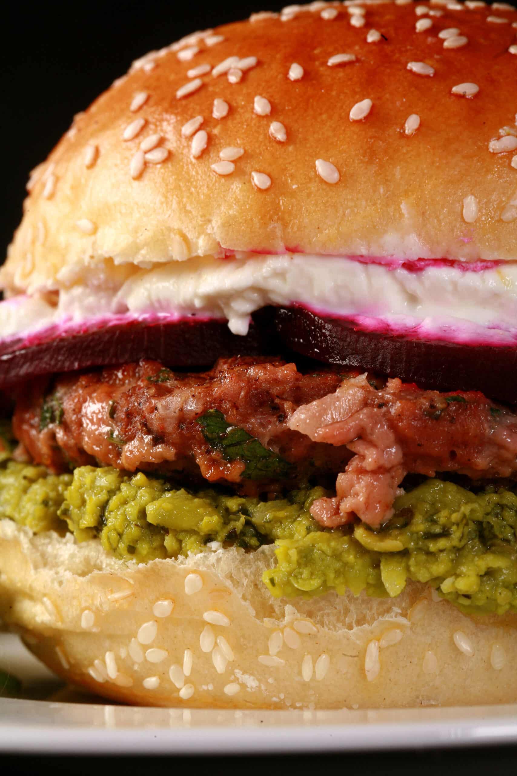 A Middle eastern spiced beyond burger with pea hummus, beet slices, and goat cheese, on a sesame bun.