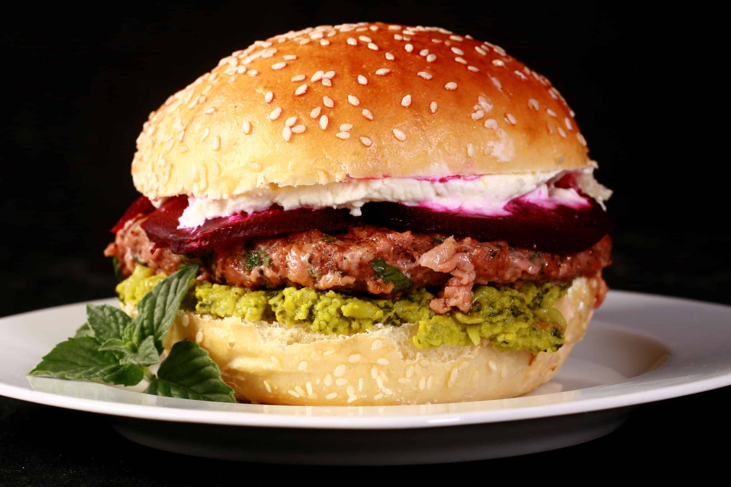 A spiced vegetarian burger with pea hummus, beet slices, and goat cheese, on a sesame bun.